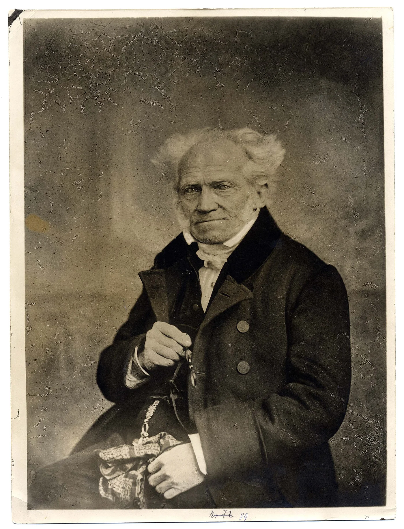 Schopenhauer sits in a dark coat with his hands in front of him