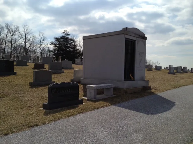 Clyfford Still's small stone mausoleum beside headstones and a cemetery road under a cloudy Maryland sky