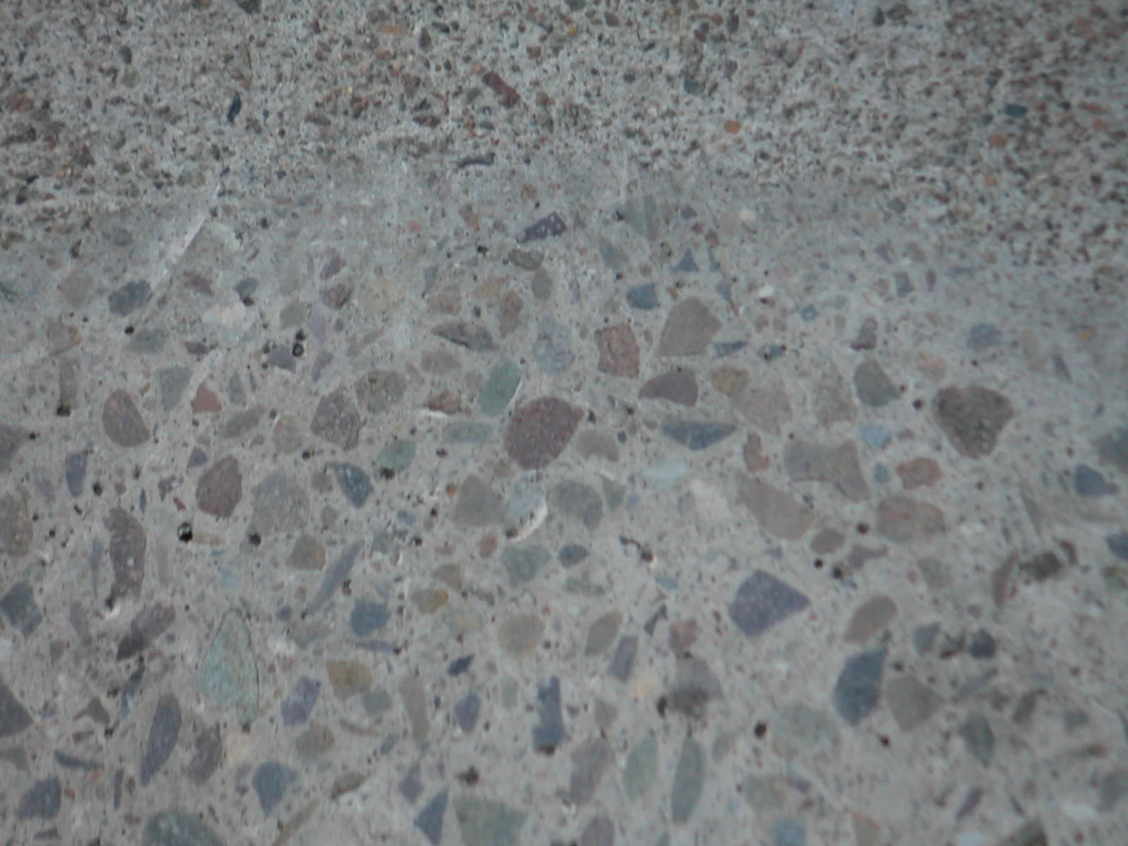Ground concrete revealing pale and dark gravel fragments within a grey cement matrix
