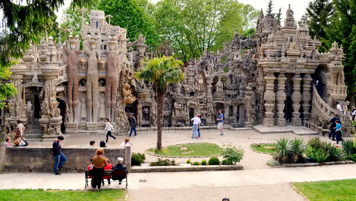 The east facade of Cheval’s Palais idéal, with clustered stone forms, towers, niches and figures in a garden