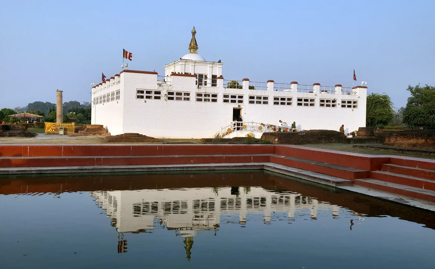 White Maya Devi Temple at Lumbini with its flat roof, surrounded by lawn, brick ruins and prayer flags