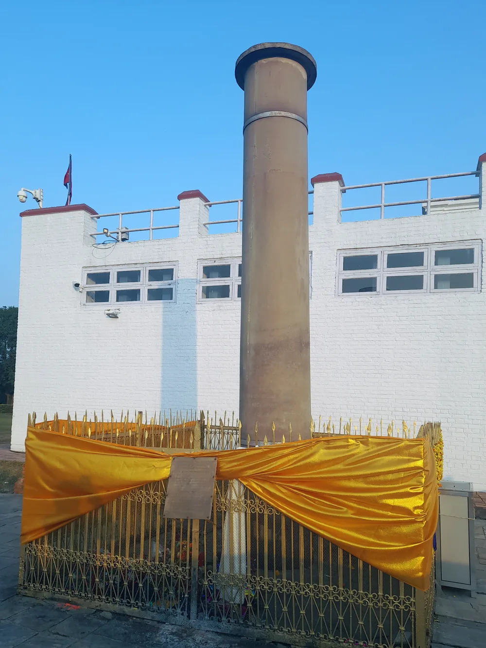 The Ashoka pillar at Lumbini, a smooth sandstone column behind a low railing, with the Maya Devi Temple behind