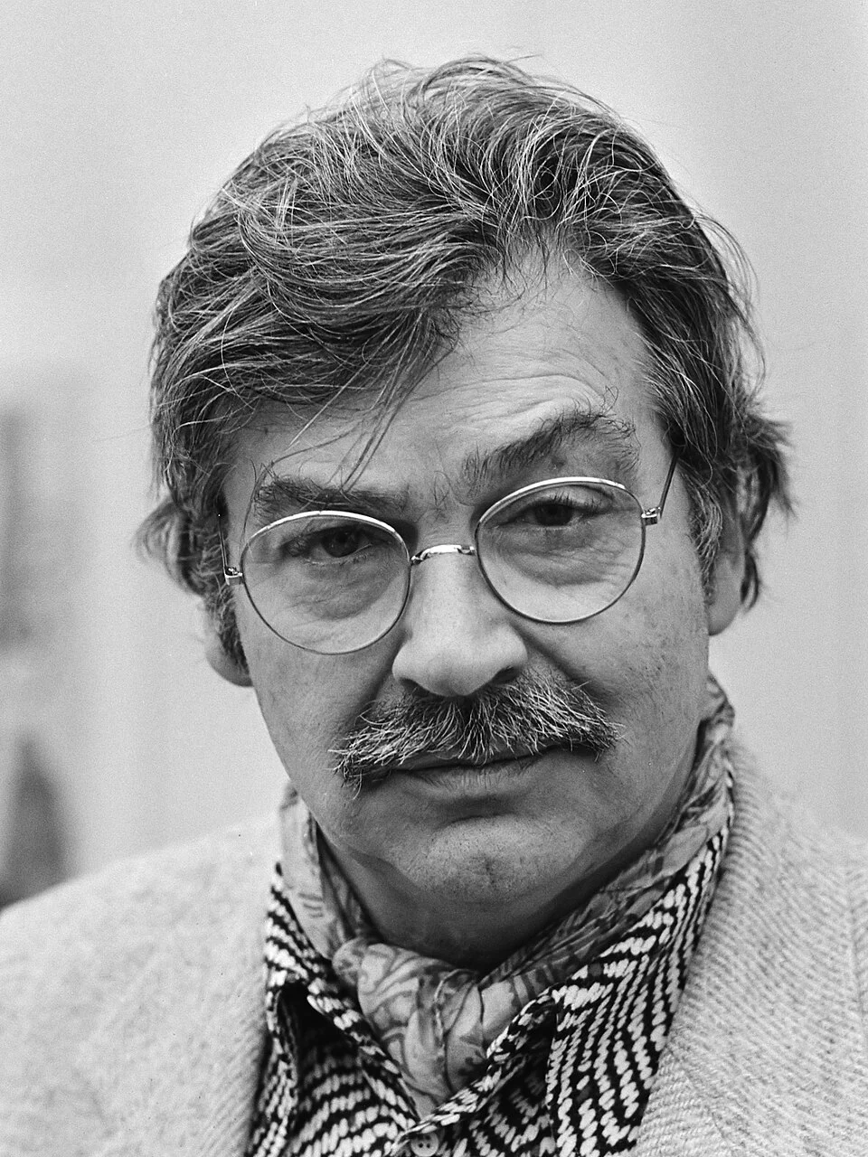 A black-and-white portrait of Karel Appel wearing glasses, a patterned scarf and a tweed jacket.