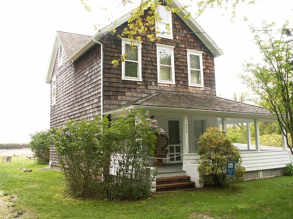 The shingled Pollock-Krasner house in Springs, New York, with a white porch, trees and a lawn.