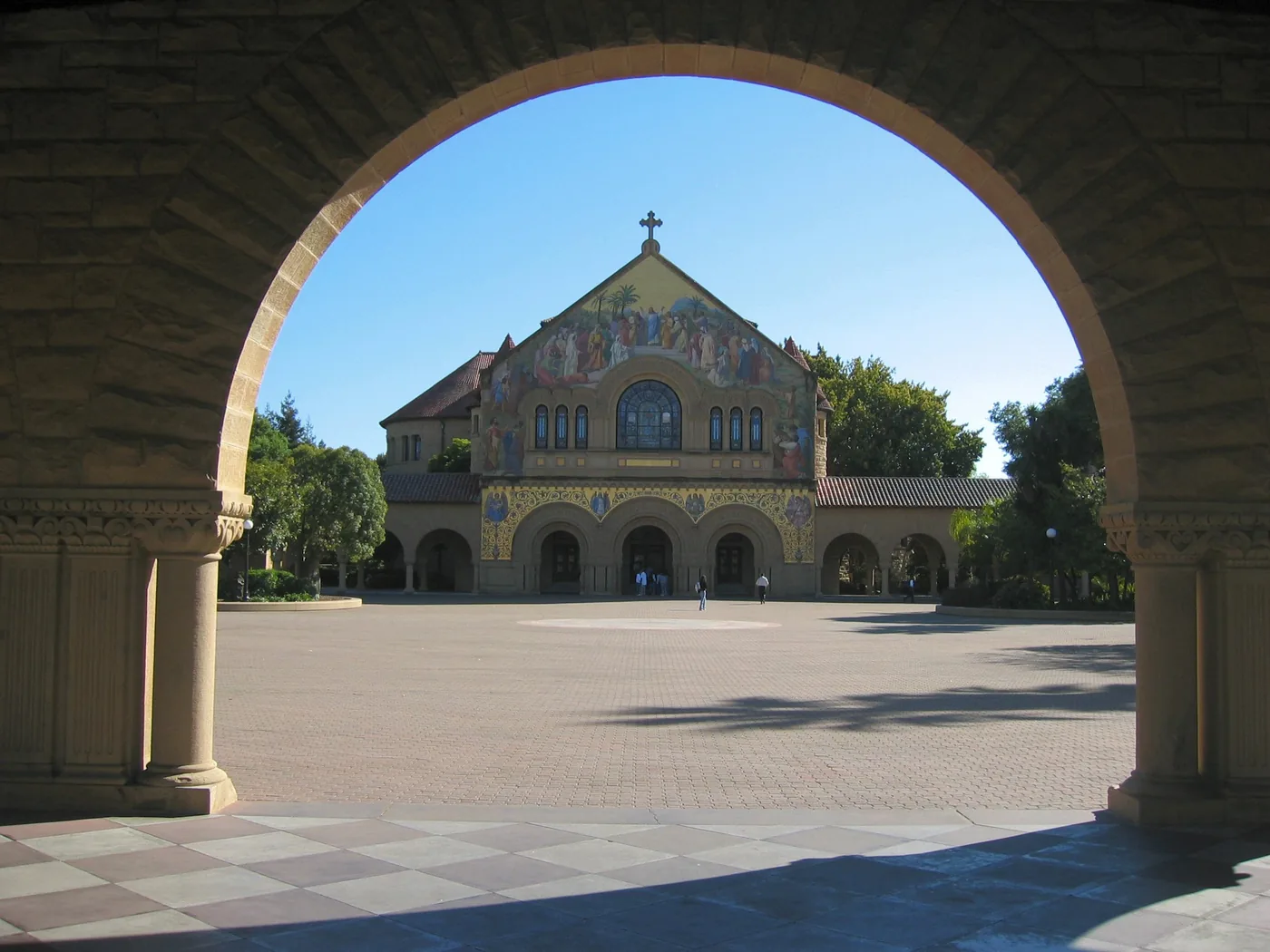 Sandstone arcades of the Stanford University Main Quad with Memorial Church at the end under a blue sky