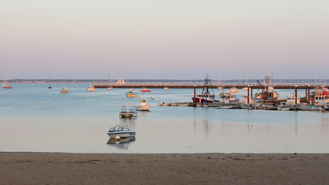 Provincetown harbour at low tide with moored boats, a long pier and the town along the shore